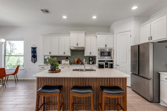 1314 Overture Pl, Round Rock, TX 78681 - kitchen with stainless steel appliances, a sink, under cabinet range hood, white cabinetry, and decorative backsplash