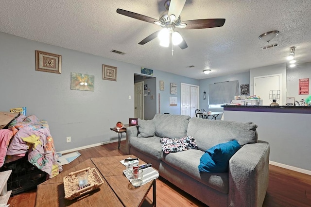 living room featuring a textured ceiling, wood finished floors, ceiling fan, and baseboards