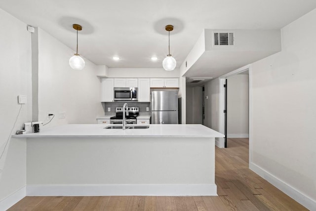 909 Reinli St Unit 101, Austin, TX 78751 - kitchen featuring stainless steel appliances, a peninsula, light countertops, white cabinetry, and hanging light fixtures