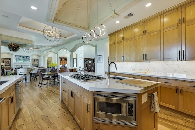 kitchen with a sink, stainless steel appliances, open floor plan, an island with sink, and arched walkways