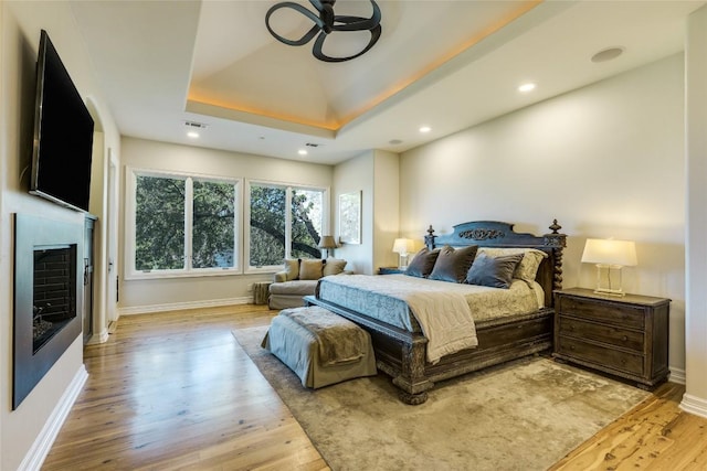 bedroom featuring light wood-type flooring, a tray ceiling, baseboards, and recessed lighting