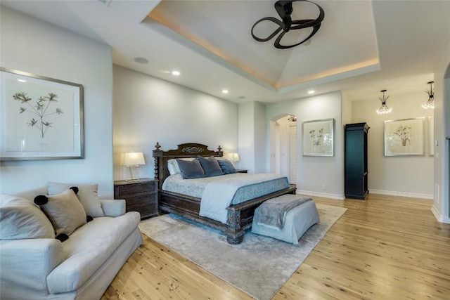 bedroom featuring a tray ceiling, arched walkways, light wood-style flooring, recessed lighting, and baseboards