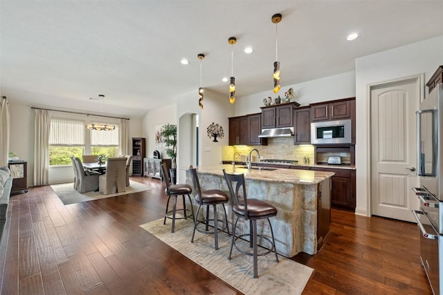 100 Royal Oak Dr, Georgetown, TX 78628 - kitchen featuring stainless steel microwave, fridge, a kitchen island with sink, decorative backsplash, and dark brown cabinetry