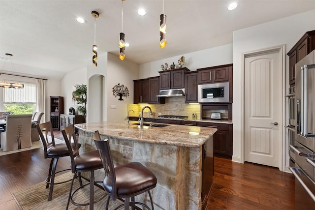 100 Royal Oak Dr, Georgetown, TX 78628 - kitchen with stainless steel microwave, under cabinet range hood, decorative backsplash, a sink, and a breakfast bar