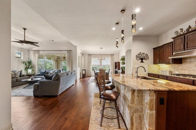 100 Royal Oak Dr, Georgetown, TX 78628 - kitchen with under cabinet range hood, a sink, arched walkways, light stone counters, and open floor plan