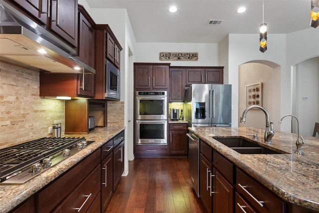 100 Royal Oak Dr, Georgetown, TX 78628 - kitchen with appliances with stainless steel finishes, a sink, under cabinet range hood, arched walkways, and dark wood finished floors