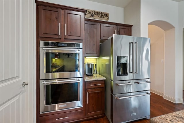100 Royal Oak Dr, Georgetown, TX 78628 - kitchen with appliances with stainless steel finishes, dark wood-type flooring, light stone countertops, baseboards, and dark brown cabinetry