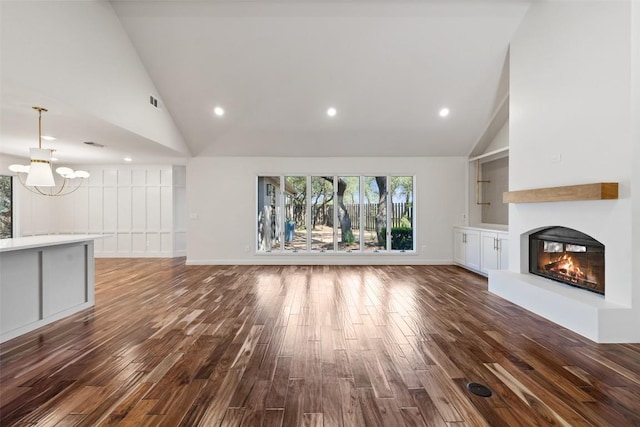 unfurnished living room with a chandelier, high vaulted ceiling, a glass covered fireplace, dark wood-style flooring, and recessed lighting
