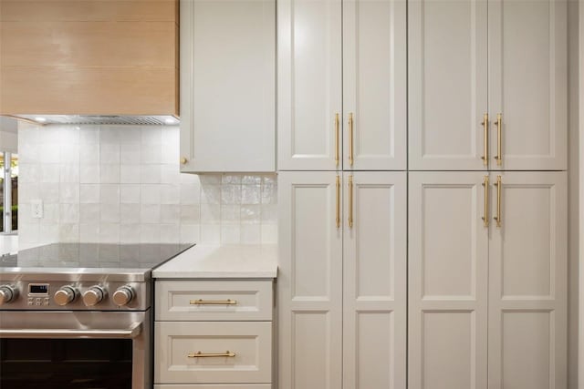 kitchen with high end range, tasteful backsplash, custom range hood, and white cabinetry