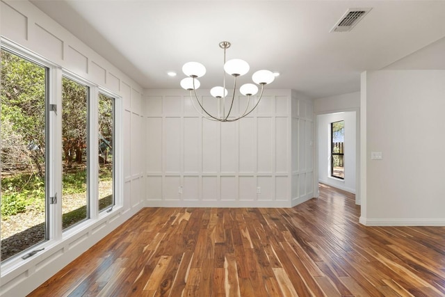 unfurnished dining area featuring hardwood / wood-style flooring, a chandelier, baseboards, and a decorative wall