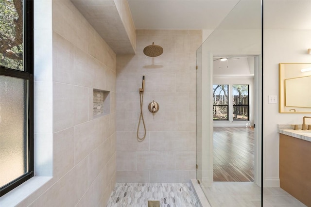 full bathroom featuring a tile shower, vanity, and a ceiling fan