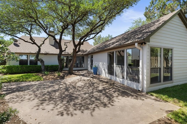back of house featuring a patio, a shingled roof, and a chimney