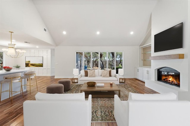 living room with high vaulted ceiling, a glass covered fireplace, recessed lighting, wood finished floors, and baseboards