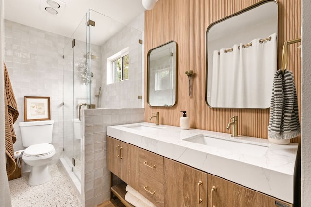 full bath with a stall shower, toilet, double vanity, speckled floor, and tile walls