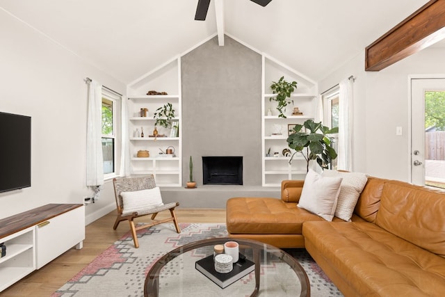 living area featuring ceiling fan, light wood-style flooring, a large fireplace, built in shelves, and baseboards