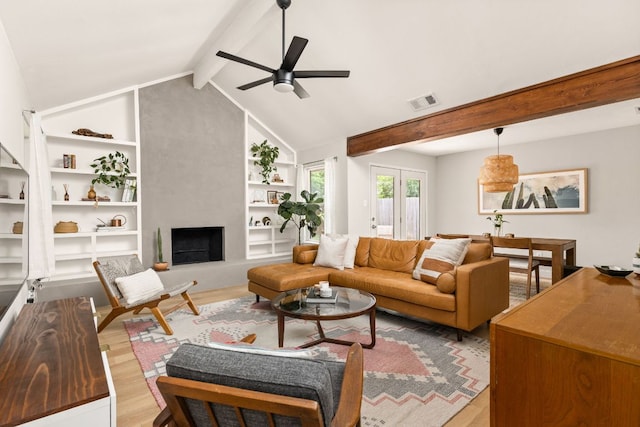living area featuring wood finished floors, a large fireplace, built in features, and a ceiling fan