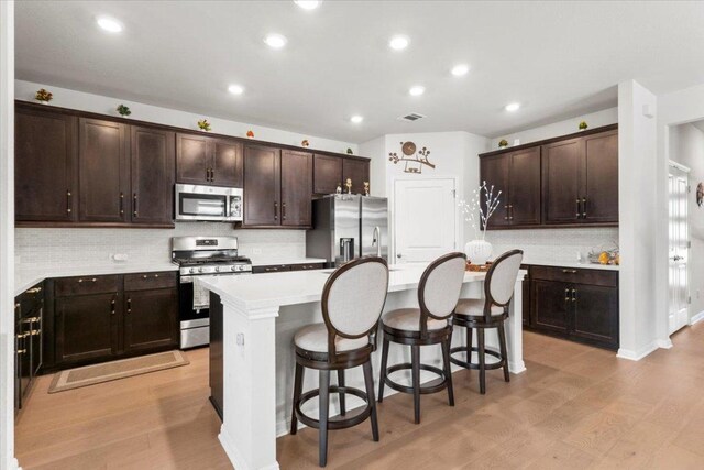 128 Green Knoll Ln, Georgetown, TX 78628 - kitchen featuring stainless steel appliances, an island with sink, a breakfast bar area, dark brown cabinetry, and light wood finished floors