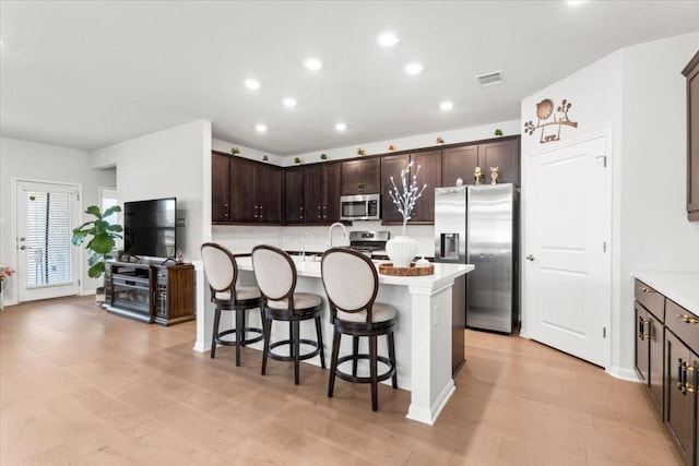 128 Green Knoll Ln, Georgetown, TX 78628 - kitchen featuring stainless steel appliances, dark brown cabinets, a kitchen island with sink, a breakfast bar area, and light wood finished floors