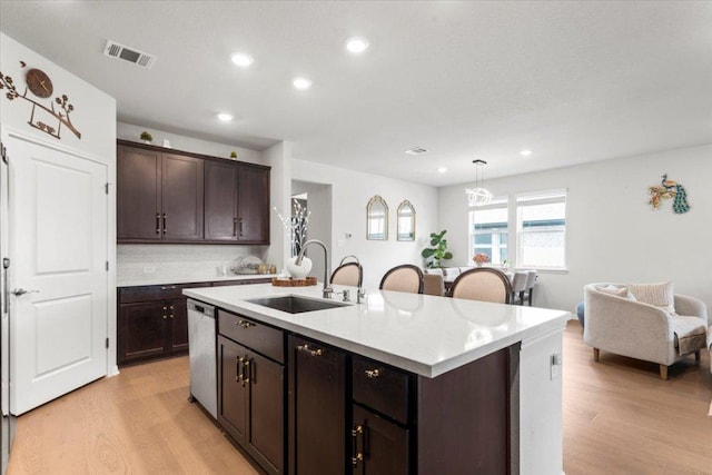 128 Green Knoll Ln, Georgetown, TX 78628 - kitchen with stainless steel dishwasher, light wood finished floors, light countertops, dark brown cabinetry, and a kitchen island with sink
