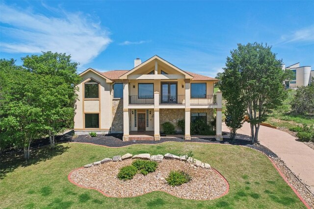 view of front of property with a balcony, stone siding, stucco siding, a chimney, and a front yard