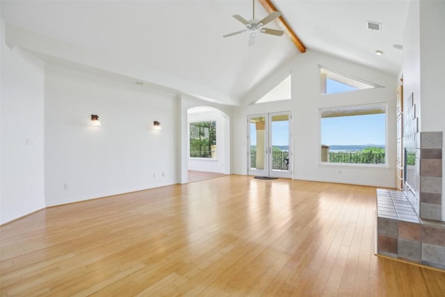 unfurnished living room featuring arched walkways, beam ceiling, plenty of natural light, ceiling fan, and light wood-type flooring
