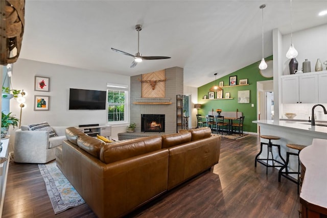 living room featuring vaulted ceiling, ceiling fan, dark wood-style flooring, and a brick fireplace