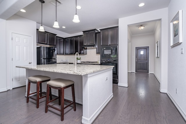 212 Beretta Cir, Georgetown, TX 78628 - kitchen featuring black appliances, decorative backsplash, dark wood-type flooring, light stone counters, and a center island with sink