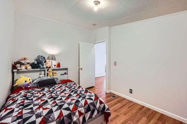 bedroom featuring wood finished floors, crown molding, and a textured ceiling