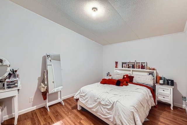 bedroom with wood finished floors, ornamental molding, a textured ceiling, and baseboards