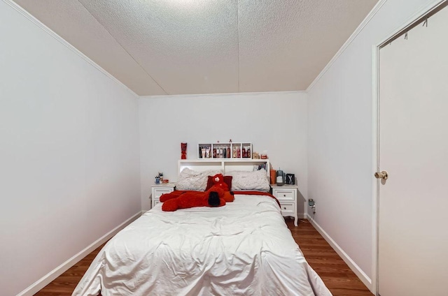 bedroom with a textured ceiling, ornamental molding, dark wood-style floors, and baseboards