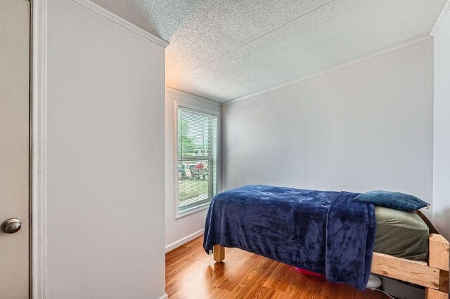 bedroom with crown molding, wood finished floors, a textured ceiling, and baseboards