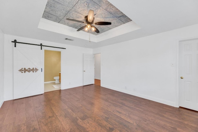 127 Edison Dr, Hutto, TX 78634 - unfurnished bedroom featuring a tray ceiling, a barn door, wood finished floors, and baseboards