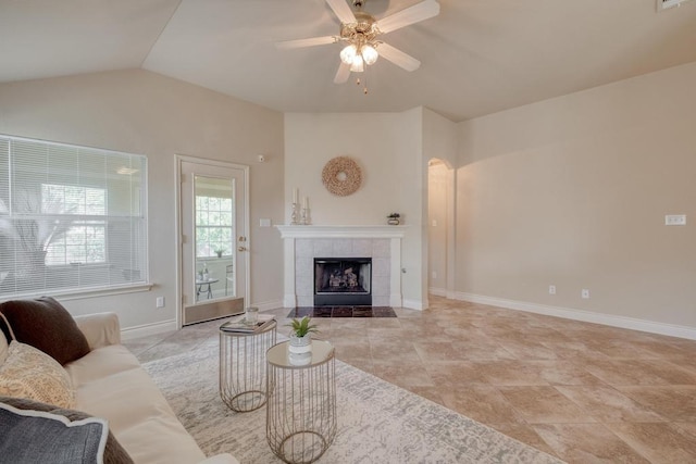 living area with a ceiling fan, vaulted ceiling, a tiled fireplace, and baseboards