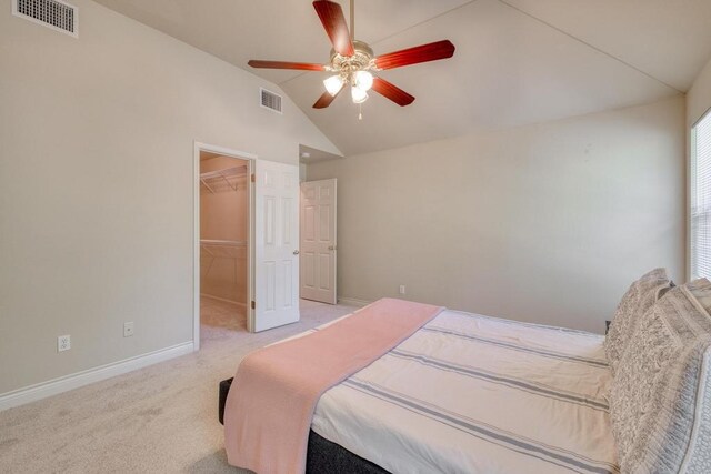 bedroom with vaulted ceiling, baseboards, a walk in closet, light carpet, and a ceiling fan