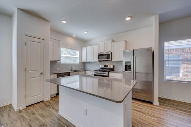 kitchen with appliances with stainless steel finishes, a sink, light wood-style flooring, white cabinets, and tasteful backsplash