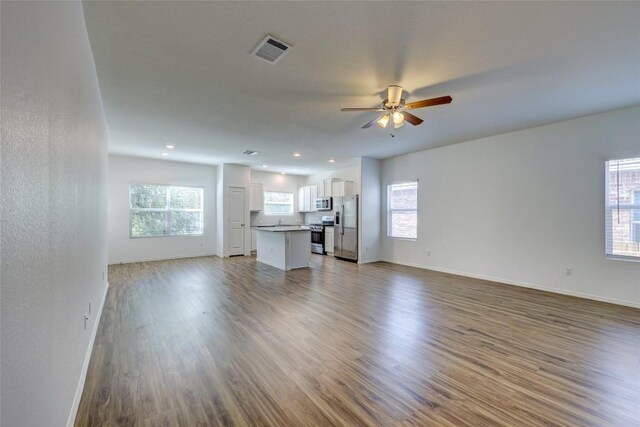 unfurnished living room with healthy amount of natural light, a ceiling fan, wood finished floors, baseboards, and recessed lighting