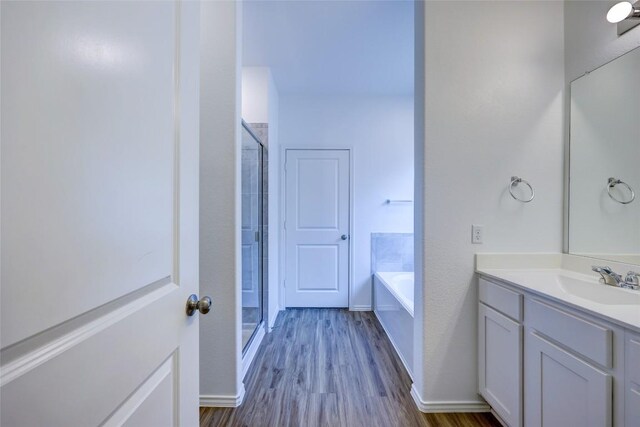 full bath featuring wood finished floors, a shower stall, a garden tub, vanity, and baseboards