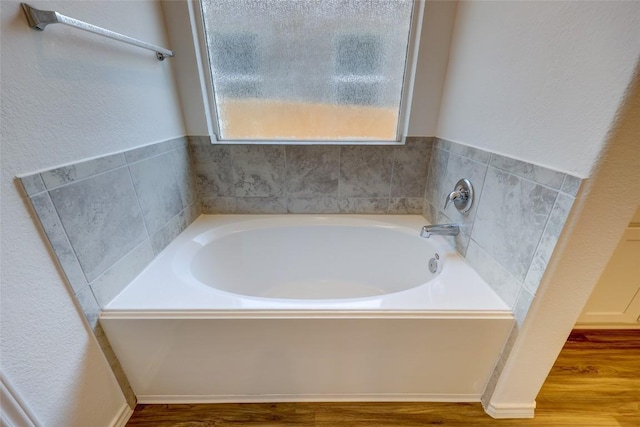 full bath featuring wood finished floors, a bath, and a textured wall