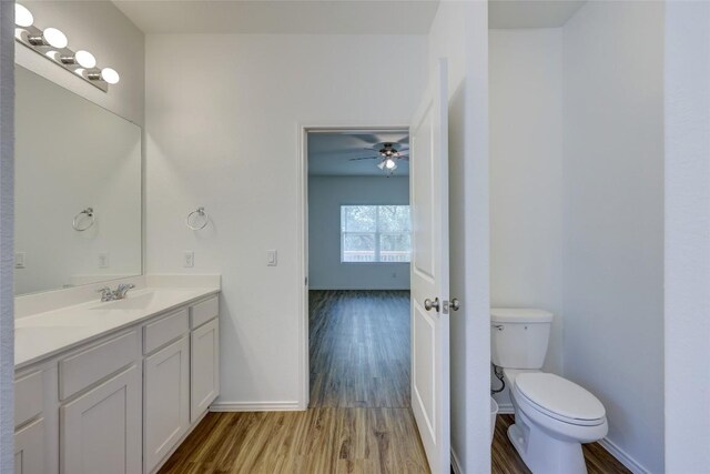 bathroom with wood finished floors, toilet, a ceiling fan, vanity, and baseboards