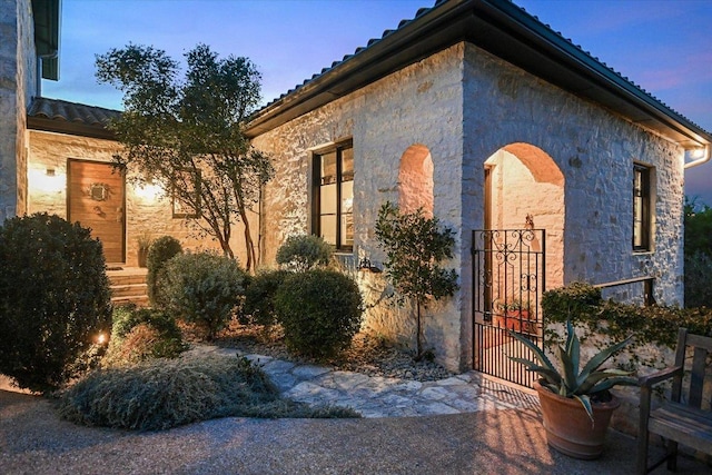 698 Windsong Trl, West Lake Hills, TX 78746 - exterior entry at dusk with stone siding, a tile roof, and a gate