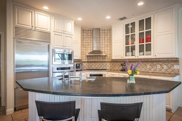kitchen featuring built in appliances, wall chimney range hood, white cabinetry, backsplash, and recessed lighting