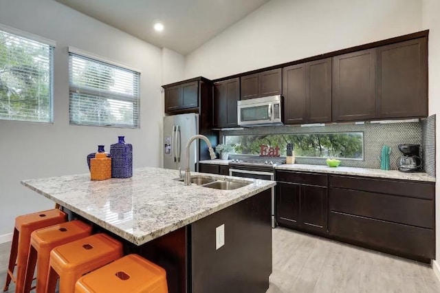 kitchen featuring appliances with stainless steel finishes, a sink, tasteful backsplash, and light wood-style flooring
