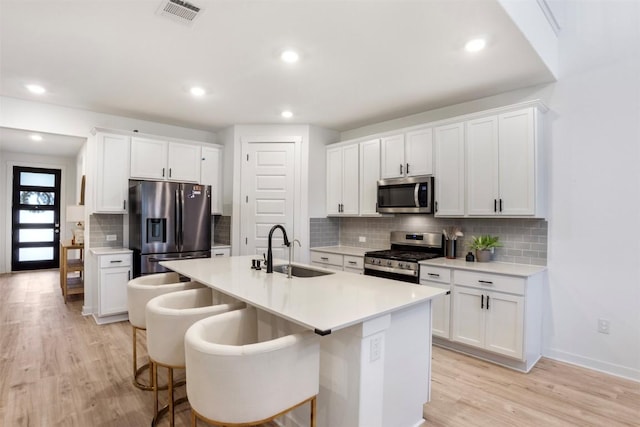 kitchen with a sink, appliances with stainless steel finishes, backsplash, light wood-type flooring, and white cabinetry