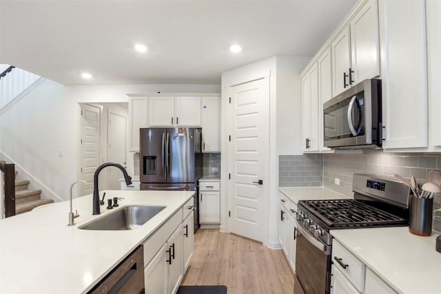 kitchen with appliances with stainless steel finishes, a sink, light countertops, white cabinetry, and recessed lighting