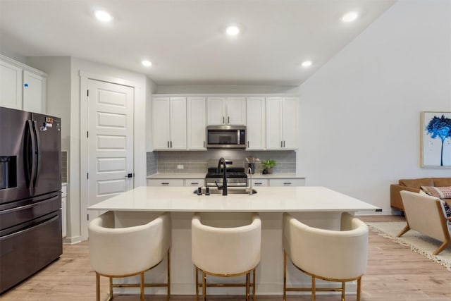 kitchen featuring appliances with stainless steel finishes, a sink, light wood-style floors, backsplash, and light countertops