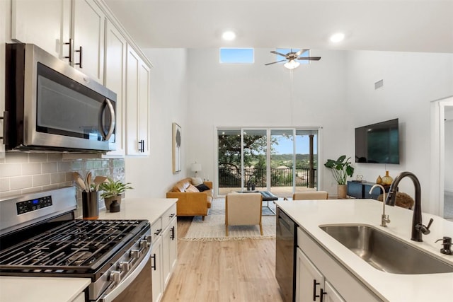 kitchen featuring appliances with stainless steel finishes, a sink, open floor plan, a high ceiling, and ceiling fan