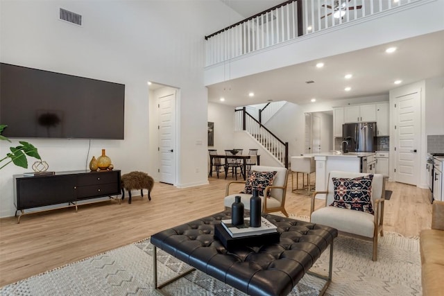 living area featuring stairway, a towering ceiling, light wood-style flooring, and recessed lighting