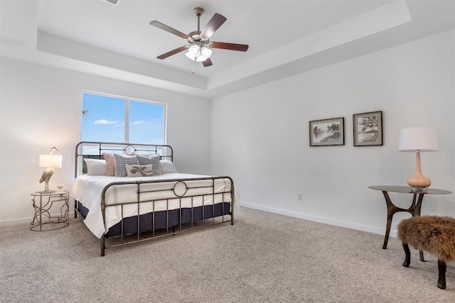 bedroom featuring a raised ceiling, carpet, baseboards, and a ceiling fan