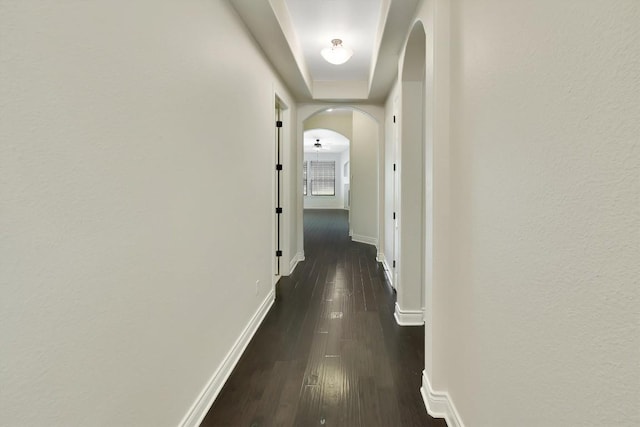 hallway with arched walkways, dark wood-style floors, and baseboards