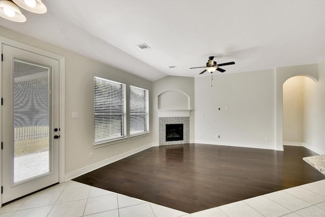 unfurnished living room with wood finished floors, a ceiling fan, a tiled fireplace, arched walkways, and baseboards